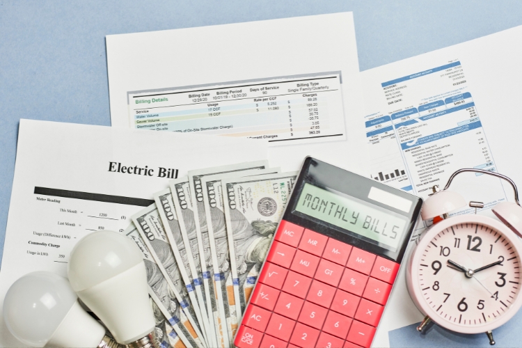 bills, calculator, money, bulb and clock on table